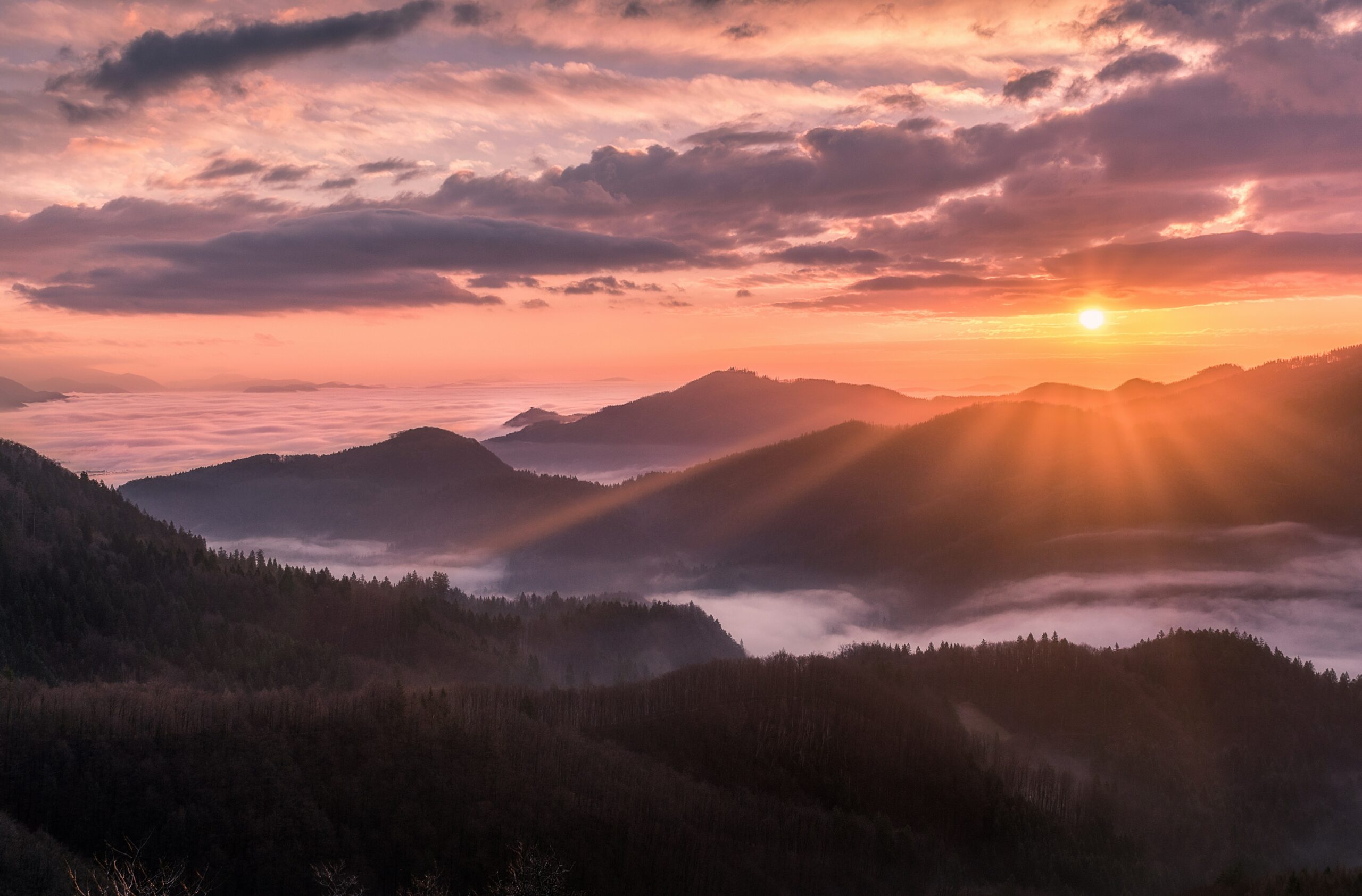 Sun setting in the clouds behind a valley surrounded by mountains